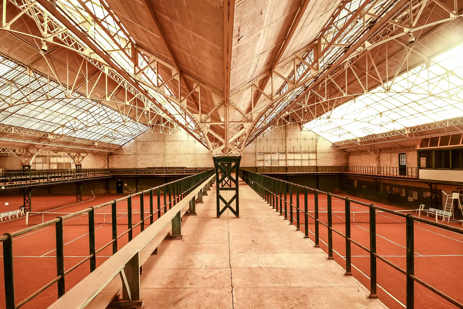 Coursive centrale suspendue entre deux courts de tennis, garde-corps métalliques et bancs de bois