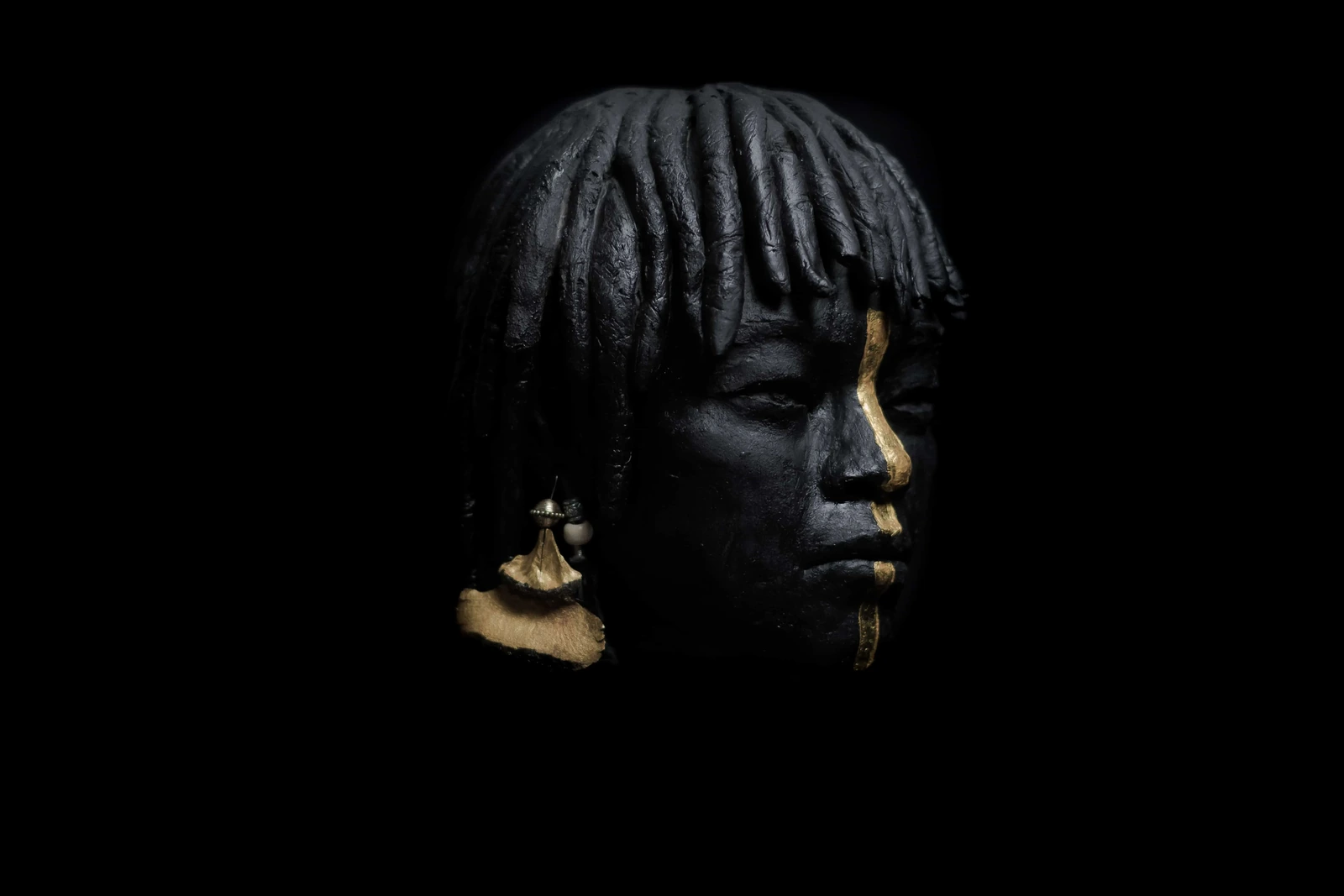 Même sculpture vue de profil, la feuille d'or courant le long de la joue, boucle d'oreille dorée